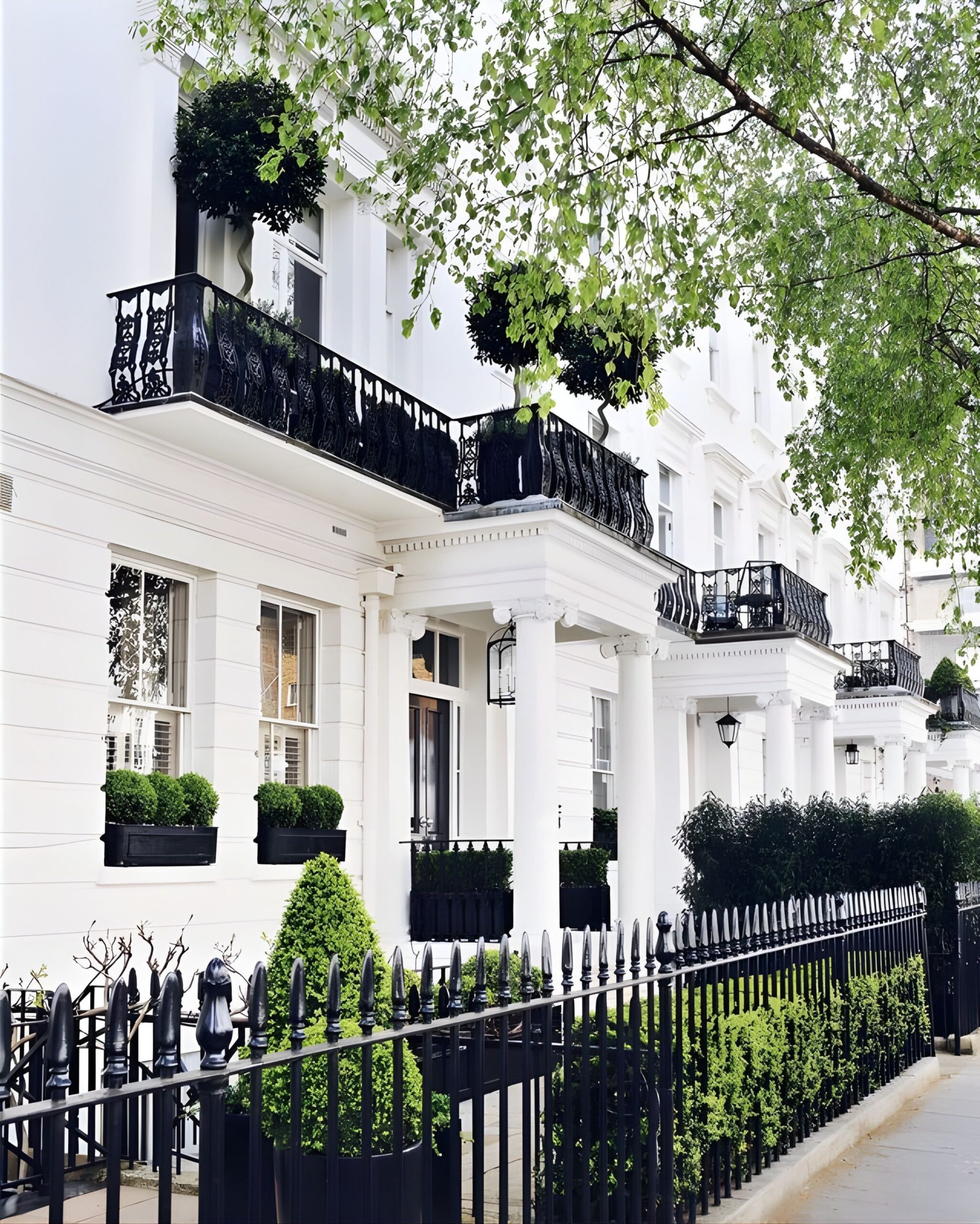 White Georgian townhouse exterior with black wrought iron balconies, front railings and manicured greenery
